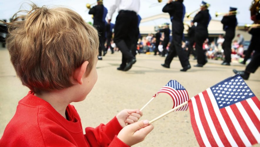 Young boy waving an American flag and watching a parade pass by