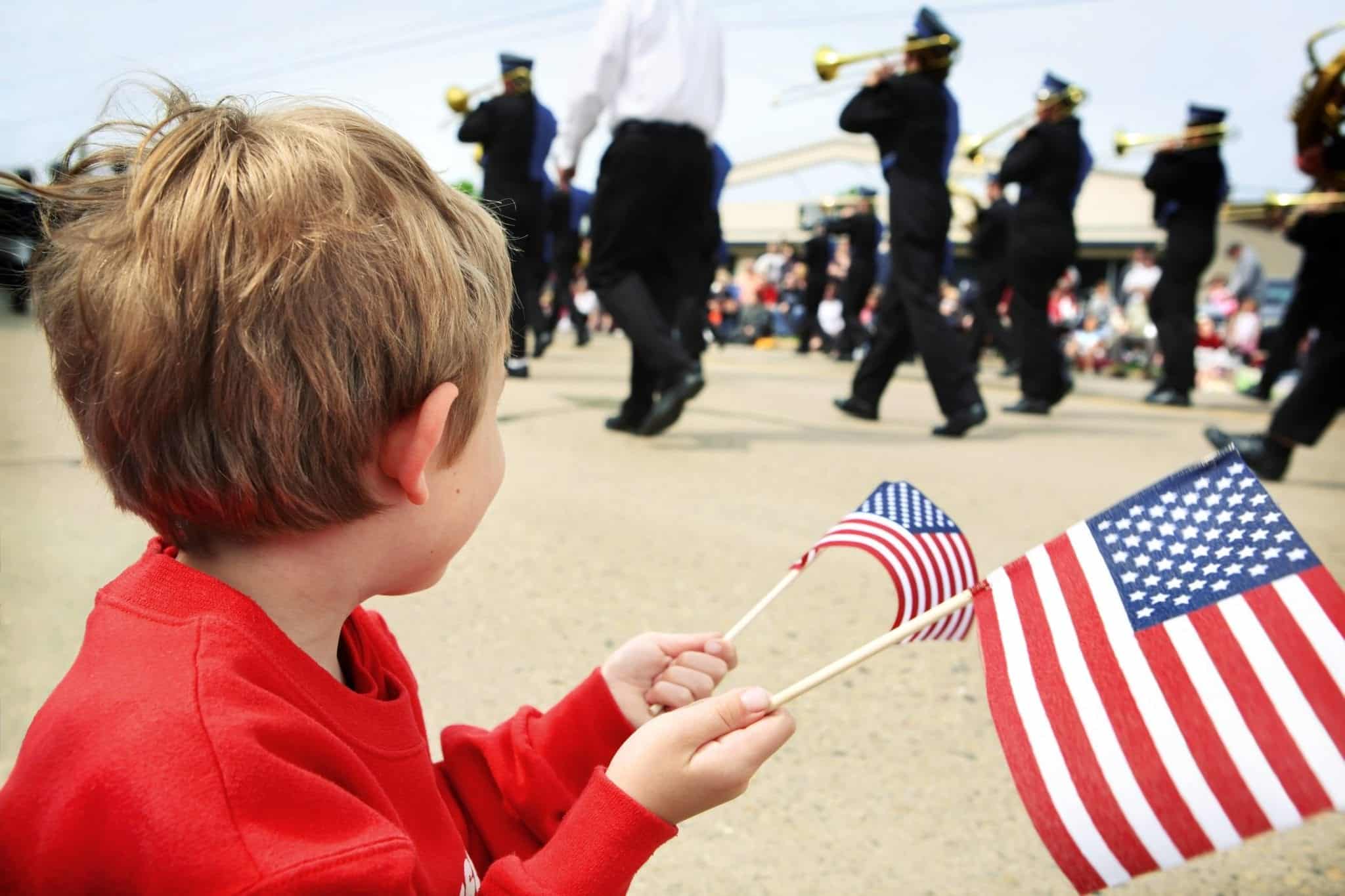 Young boy waving an American flag and watching a parade pass by