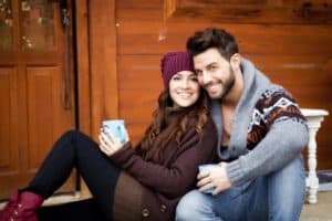 Couple sitting outside of a cabin sipping on a hot beverage
