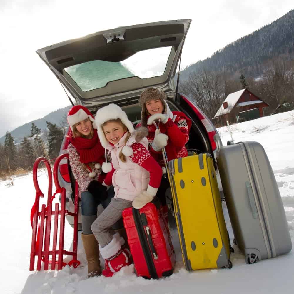 Three kids in the back of a car with luggage, surrounded by snow