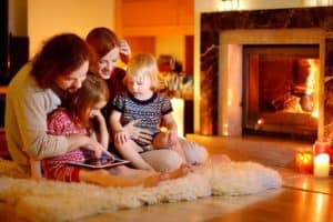 A young family reading together on a rug in front of the fireplace.