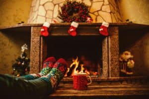 Someone wearing holiday socks relaxing in front of the Christmas decorated fireplace with a mug of hot chocolate.