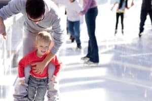 A father and son ice skating at a rink.