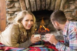 Happy couple drinking coffee in front of the fireplace in their cabin.