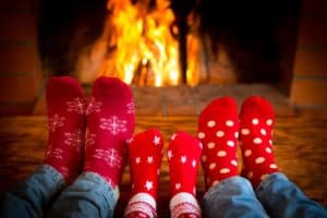 Three pairs of feet in socks relaxing in front of the fireplace.