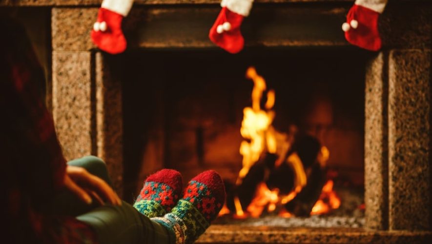 A woman warming her feet beside a fireplace in a cabin decorated for Christmas.
