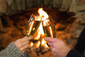 couple holding champagne glasses in front of fire