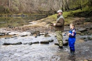 man and son catching trout in a river